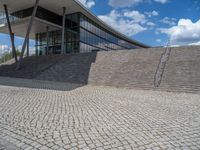 a person on a bike walking through a stone building entrance, in front of an enormous glass wall and stairs