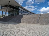 a person on a bike walking through a stone building entrance, in front of an enormous glass wall and stairs