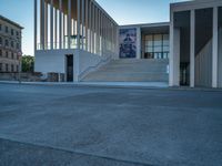 empty street lined with cement buildings next to a tall building with a staircase up to it