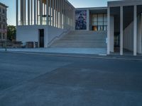 empty street lined with cement buildings next to a tall building with a staircase up to it