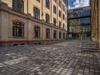 a sidewalk with chairs next to the brick building on the side, some have stairs and some buildings in the background