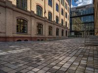 a sidewalk with chairs next to the brick building on the side, some have stairs and some buildings in the background