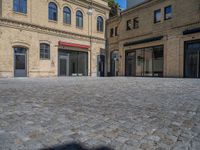 the sidewalk is paved with stones and has a bench in front of it, with no people inside