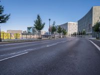 a long empty road with traffic signals near buildings along it and a railing on the other side