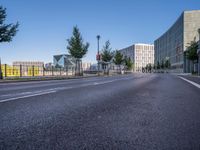 a long empty road with traffic signals near buildings along it and a railing on the other side