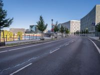 a long empty road with traffic signals near buildings along it and a railing on the other side