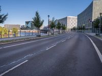 a long empty road with traffic signals near buildings along it and a railing on the other side