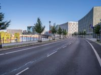 a long empty road with traffic signals near buildings along it and a railing on the other side