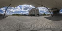 this is a fish eye lens showing a courtyard and buildings with cloudy skies and a few people