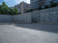 the empty parking lot in front of a wall with apartment buildings on it and a skateboarder on a ramp