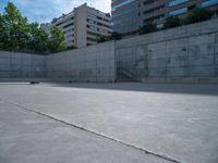 the empty parking lot in front of a wall with apartment buildings on it and a skateboarder on a ramp