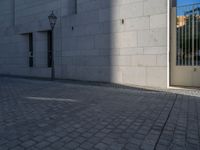 two people walking down an empty city street in an alley area with tall buildings in the background