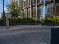 the side walk of a glass office building with concrete bricks and landscaping on each floor