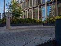 the side walk of a glass office building with concrete bricks and landscaping on each floor