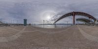 a fish - eye lens picture of the bay bridge and harbor in the background with a bench and umbrella in the foreground