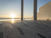 the sun set behind three large pillars and water with benches on it near the ocean