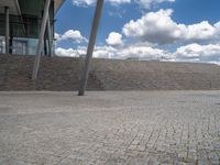 a person on a bike walking through a stone building entrance, in front of an enormous glass wall and stairs