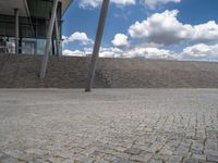 a person on a bike walking through a stone building entrance, in front of an enormous glass wall and stairs