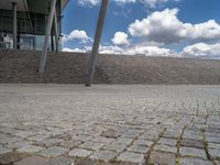 a person on a bike walking through a stone building entrance, in front of an enormous glass wall and stairs