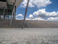 a person on a bike walking through a stone building entrance, in front of an enormous glass wall and stairs