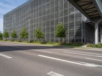 an empty street in front of a building with a glass facade and trees in the foreground