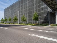 an empty street in front of a building with a glass facade and trees in the foreground