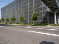 an empty street in front of a building with a glass facade and trees in the foreground