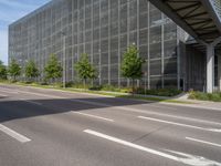 an empty street in front of a building with a glass facade and trees in the foreground