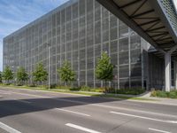 an empty street in front of a building with a glass facade and trees in the foreground