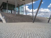 a person on a bike walking through a stone building entrance, in front of an enormous glass wall and stairs