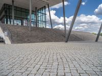 a person on a bike walking through a stone building entrance, in front of an enormous glass wall and stairs