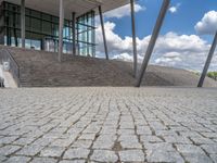 a person on a bike walking through a stone building entrance, in front of an enormous glass wall and stairs