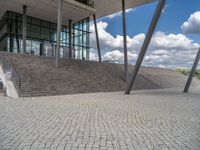 a person on a bike walking through a stone building entrance, in front of an enormous glass wall and stairs