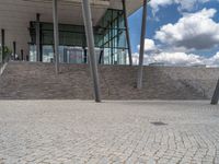 a person on a bike walking through a stone building entrance, in front of an enormous glass wall and stairs