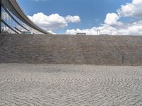 a person on a bike walking through a stone building entrance, in front of an enormous glass wall and stairs