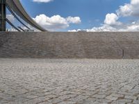 a person on a bike walking through a stone building entrance, in front of an enormous glass wall and stairs