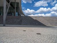 a person on a bike walking through a stone building entrance, in front of an enormous glass wall and stairs