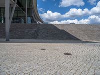 a person on a bike walking through a stone building entrance, in front of an enormous glass wall and stairs