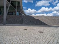 a person on a bike walking through a stone building entrance, in front of an enormous glass wall and stairs