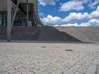 a person on a bike walking through a stone building entrance, in front of an enormous glass wall and stairs