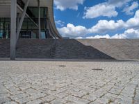 a person on a bike walking through a stone building entrance, in front of an enormous glass wall and stairs