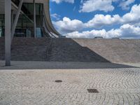 a person on a bike walking through a stone building entrance, in front of an enormous glass wall and stairs