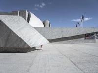 an empty cement wall in front of a red fire hydrant in concrete structure with other building on the other side