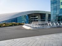 a curved structure in front of a large glass building with stairs up to the top