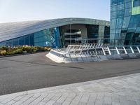 a curved structure in front of a large glass building with stairs up to the top