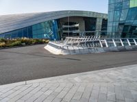 a curved structure in front of a large glass building with stairs up to the top