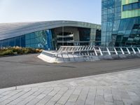 a curved structure in front of a large glass building with stairs up to the top