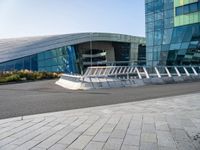 a curved structure in front of a large glass building with stairs up to the top