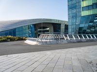 a curved structure in front of a large glass building with stairs up to the top