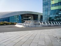 a curved structure in front of a large glass building with stairs up to the top